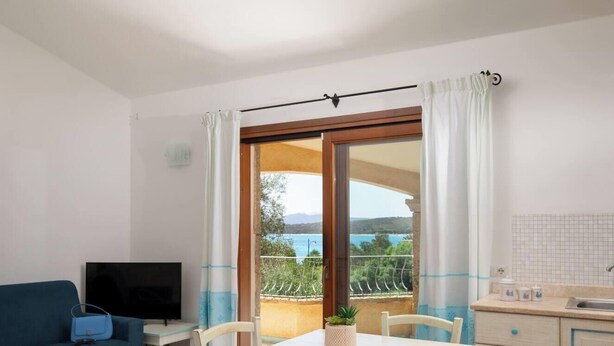A room with a balcony, a TV, a table, chairs, a sink, and a view of the sea. - Villa Azzurra by Propertize - a few steps from the sea (Pittulongu)