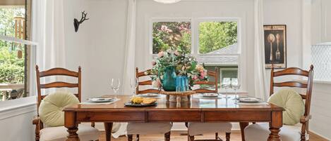 A dining room with a wooden table, chairs, a chandelier, and a window with a view of trees.