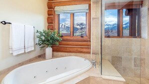 Ein Badezimmer mit einer großen Badewanne, einer Zimmerpflanze, einem Fenster mit Bergblick und Holzvertäfelung.