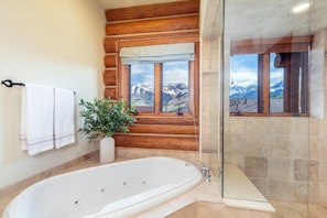 Une salle de bain avec une grande baignoire, une plante en pot, une fenêtre donnant sur les montagnes et un lambris en bois.