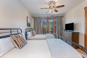 A bedroom with two beds, a ceiling fan, a television, and a view of the outdoors.