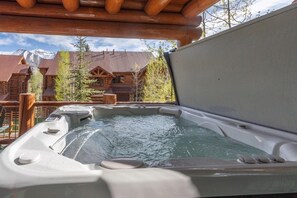 Un bain à remous avec une terrasse en bois et une vue sur un chalet de montagne.