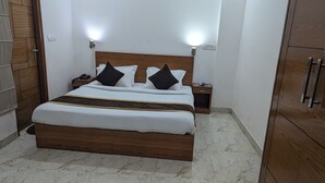 A neatly made bed with a wooden headboard, two bedside tables with lamps, and a wardrobe. - Hotel Prime Chhatarpur (New Delhi)