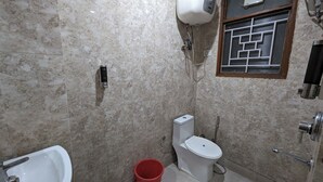 A bathroom with a toilet, bidet, and a red bucket. - Hotel Prime Chhatarpur (New Delhi)