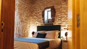 Ein Schlafzimmer mit einer Steinsäule, einem Bett mit einem dunkelgrünen Kopfteil und einem kleinen Fenster.