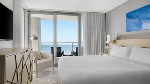 Ein Hotelzimmer mit einem großen Bett, einem Schreibtisch, einem Sessel und Blick aufs Meer.