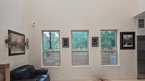 A spacious living room with a black leather sofa, a round pet bed, and three windows with wooden shutters.