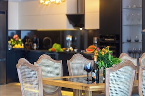 A dining area with a wooden table and wicker chairs, a vase with flowers, and a wine bottle.