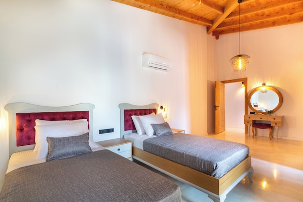 A bedroom with two beds, a wooden ceiling, an air conditioning unit, a vanity with a mirror, and a hanging light fixture.