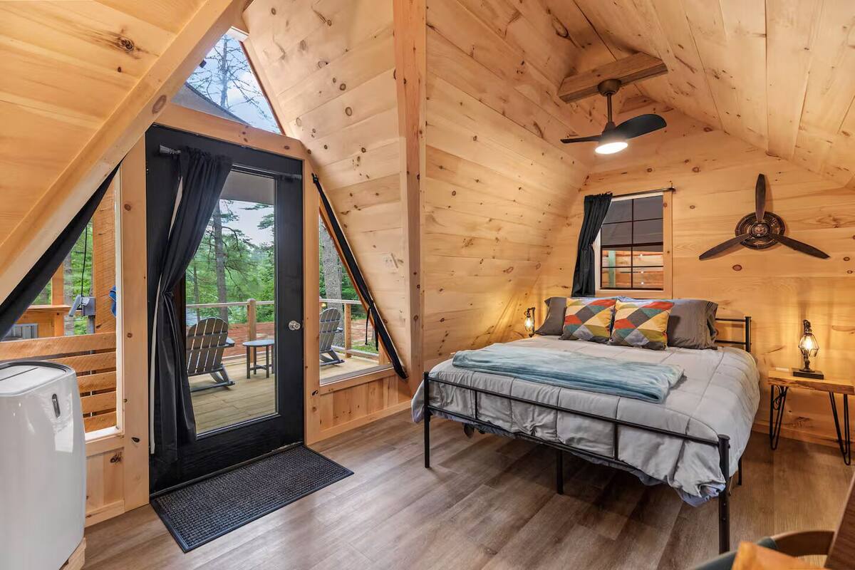 A cozy wooden cabin bedroom with a bed, a ceiling fan, and a view of the outdoors.