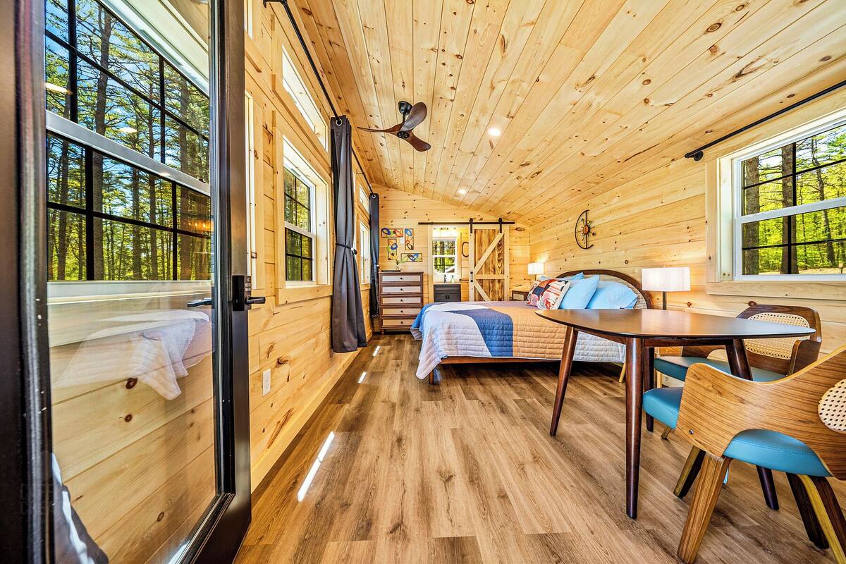A wooden cabin interior with a bed, a dining table, and a chair.