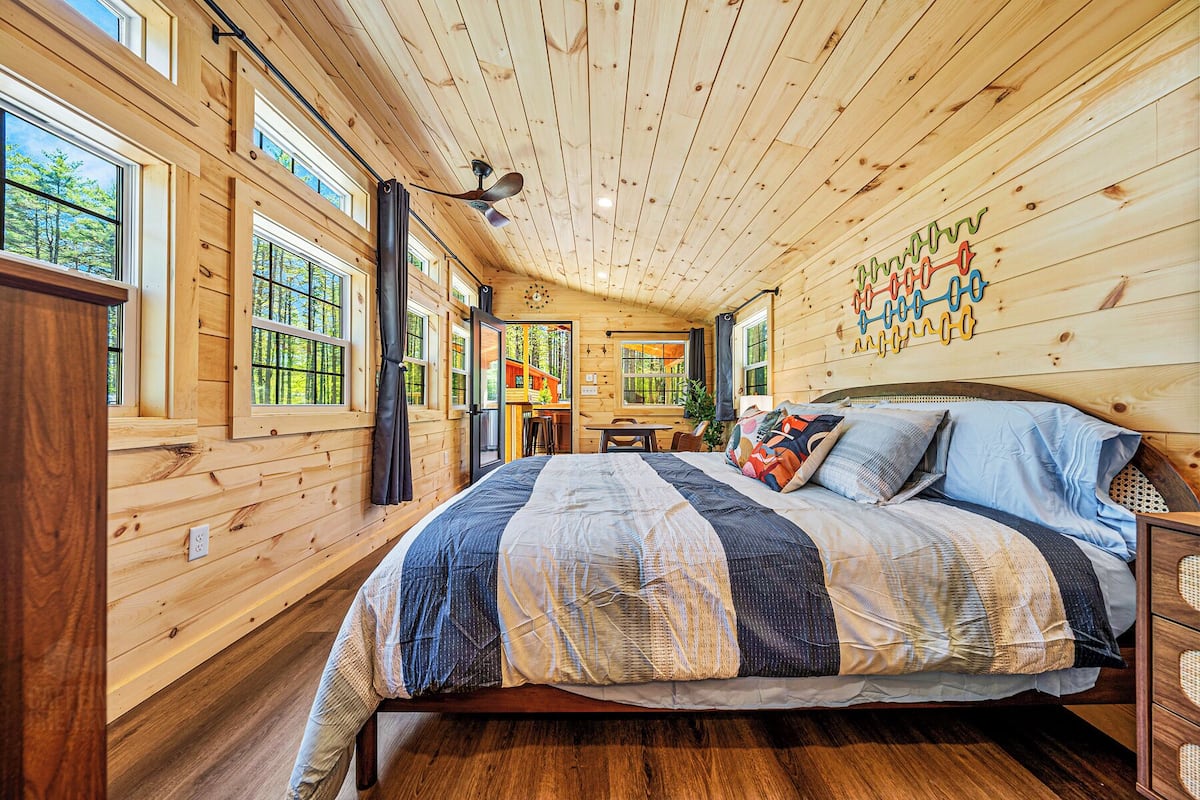 A wooden cabin bedroom with a bed, a ceiling fan, and large windows.