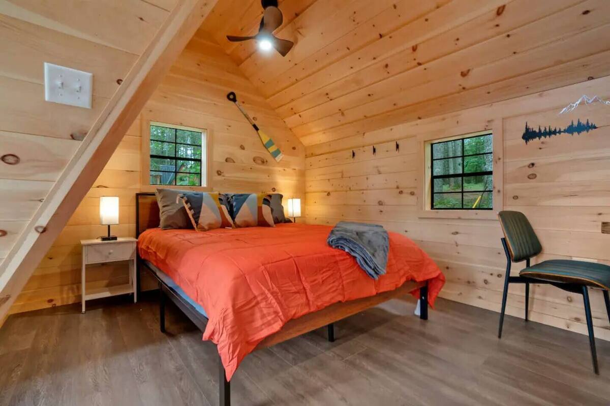 A cozy wooden cabin bedroom with a bed, nightstands, a chair, and a ceiling fan.