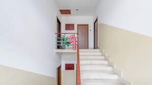 Una escalera con barandilla de madera, un objeto rojo y blanco a rayas colgando de la barandilla, y una pequeña planta en maceta en el rellano.