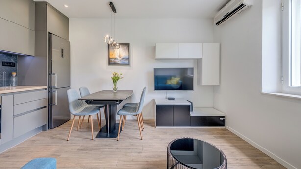 Una cocina moderna con refrigerador integrado, mesa de comedor con sillas, televisor y un pequeño rincón de estar con sofá y mesa redonda.