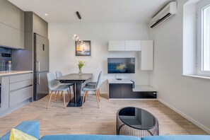 Une cuisine moderne équipée d’un réfrigérateur encastré, d’une table à manger avec des chaises, d’un téléviseur et d’un petit coin salon avec un canapé et une table ronde.