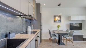 Una cocina moderna con estufa integrada, comedor con mesa y sillas, y un televisor de pantalla plana grande montado en la pared.