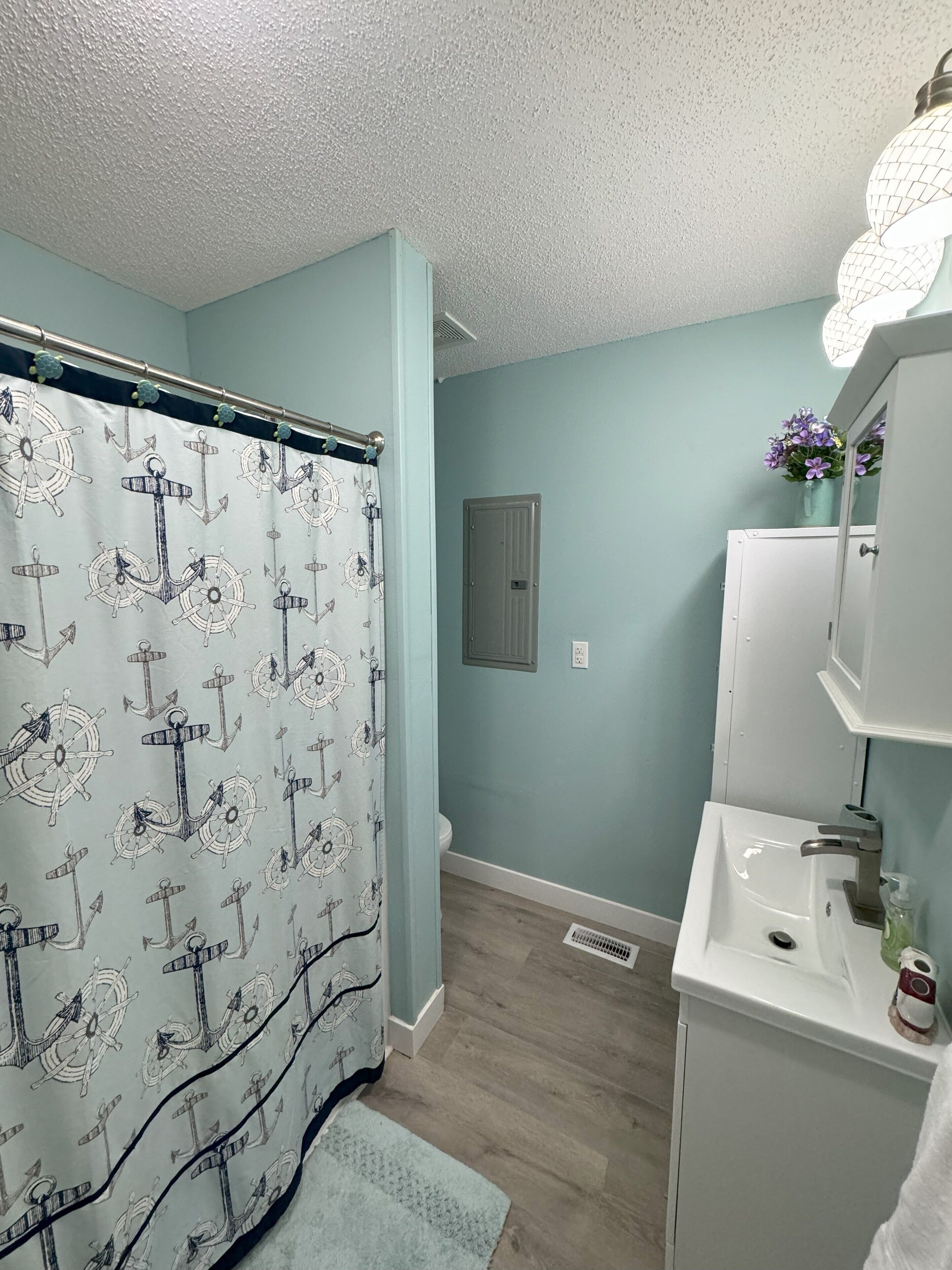 Une salle de bain avec un rideau de douche à motifs nautiques, un lavabo blanc et un miroir au-dessus.