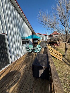 A wooden deck with a metal building, a gazebo, and a covered table and chairs area.