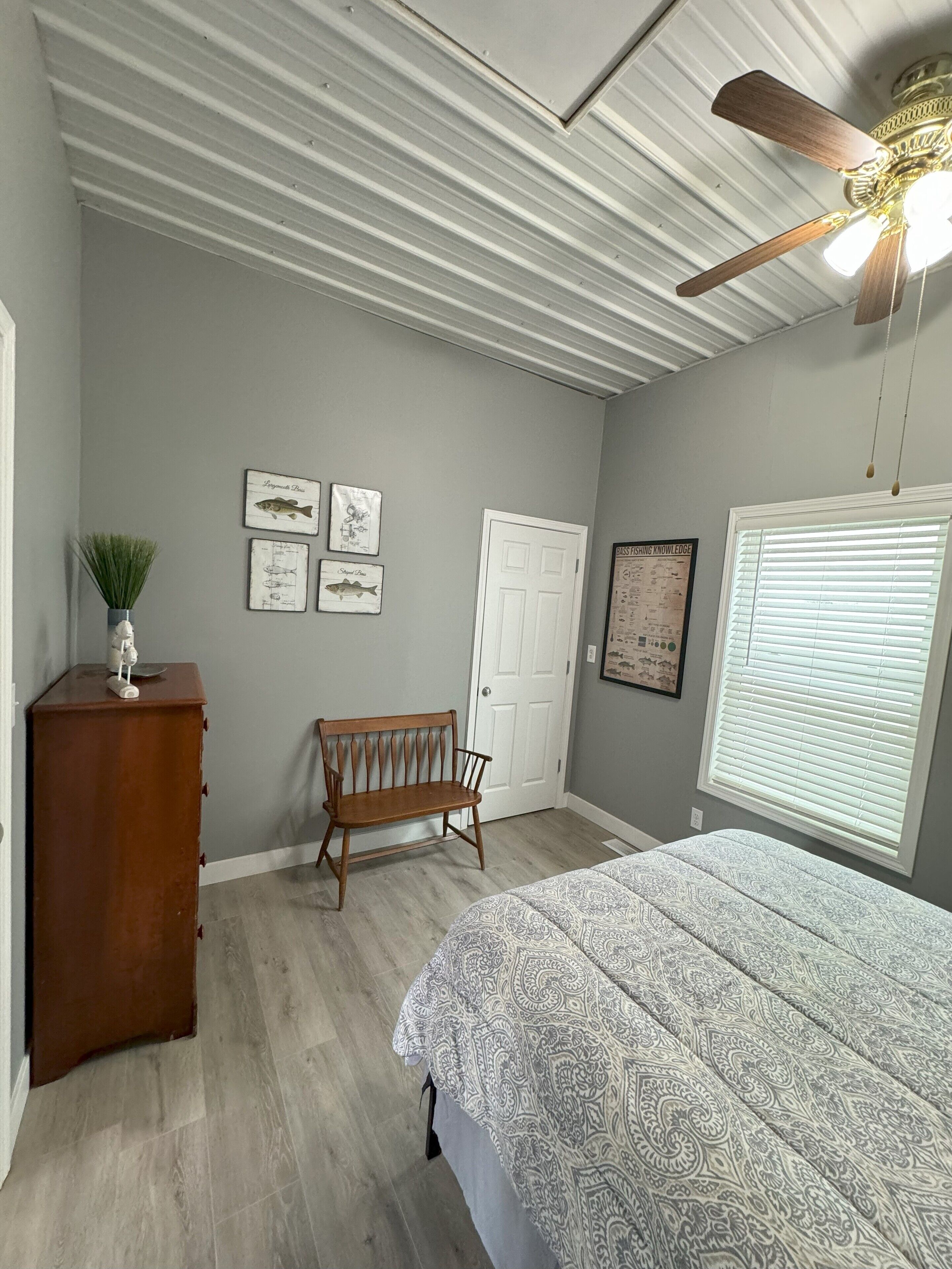 Un dormitorio con una cama, un banco de madera, un aparador y un ventilador de techo.
