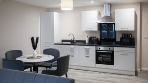 A modern kitchen with white cabinetry, a stainless steel range hood, and a black microwave. There is a round dining table with chairs and a vase with feathers.