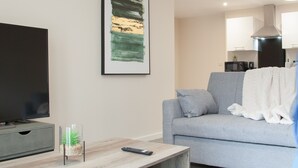 A modern living room with a flat-screen TV, a wooden coffee table, a grey sofa, and a framed abstract painting on the wall.