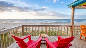 Une terrasse en bois avec des chaises rouges et une table, d’où l’on a vue sur la plage et l’océan.
