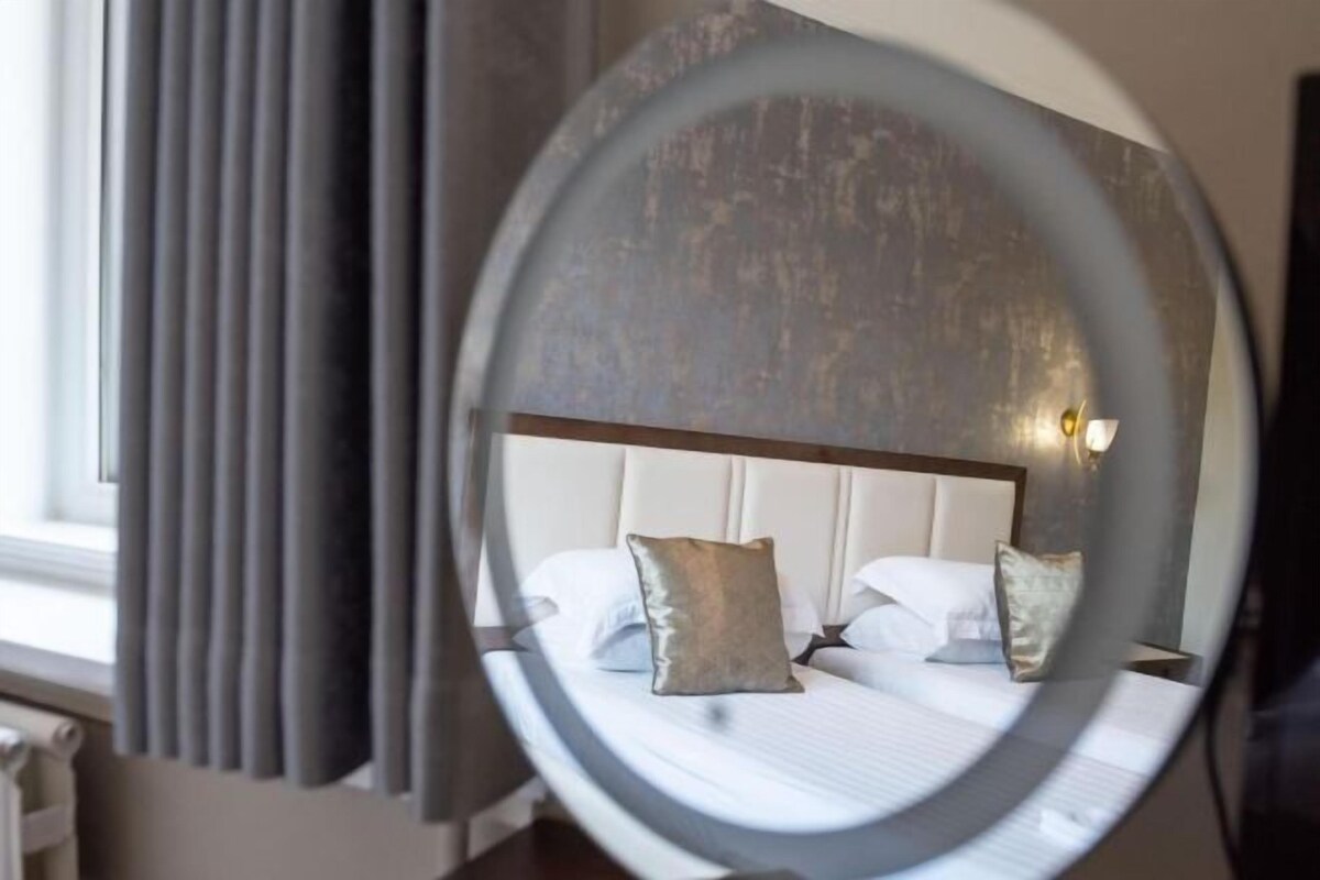 A hotel room with a bed, pillows, a headboard, and a window with curtains.