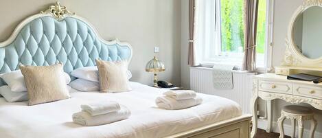 A bedroom with a tufted headboard, a bedside table with a lamp, a dresser, and a window with curtains.