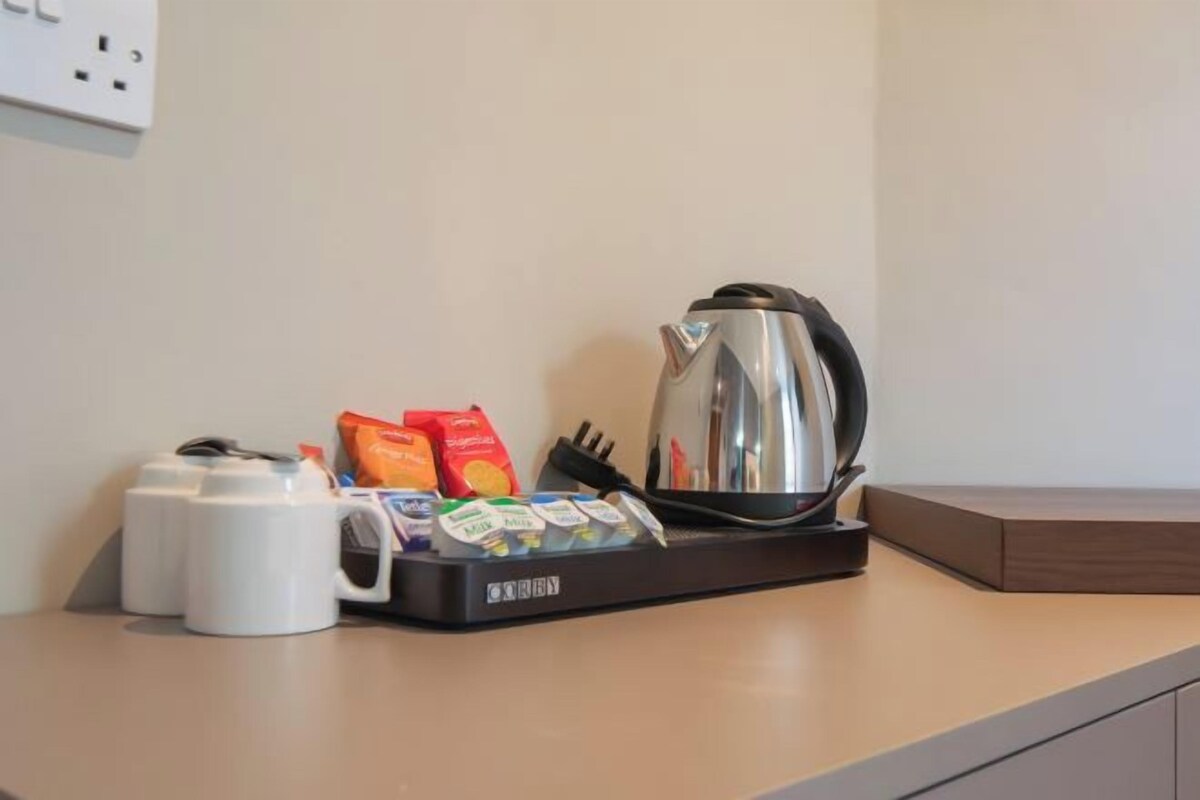 Una encimera de cocina con una cafetera, un hervidor y una bandeja con cápsulas de café y una cuchara.