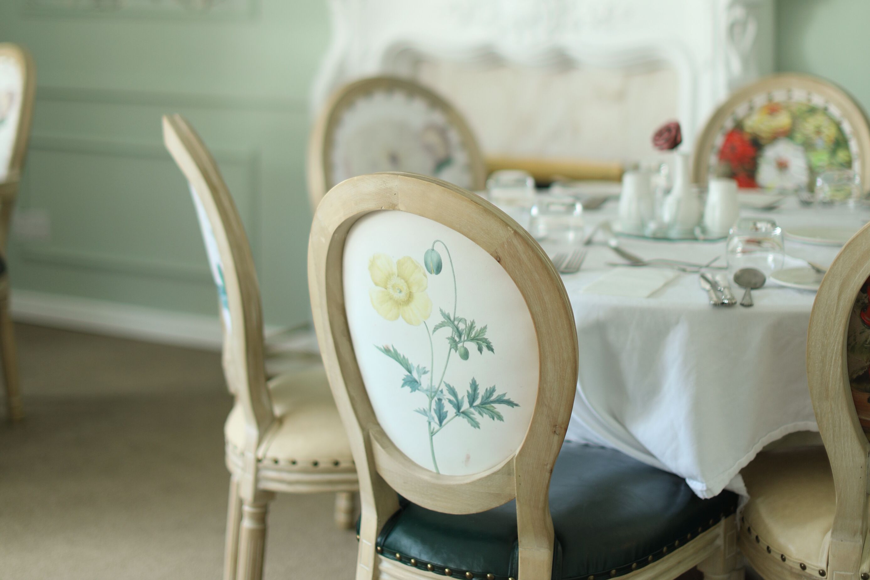 Una mesa de comedor con mantel blanco, sillas con estampado floral y una decoración de estilo antiguo.