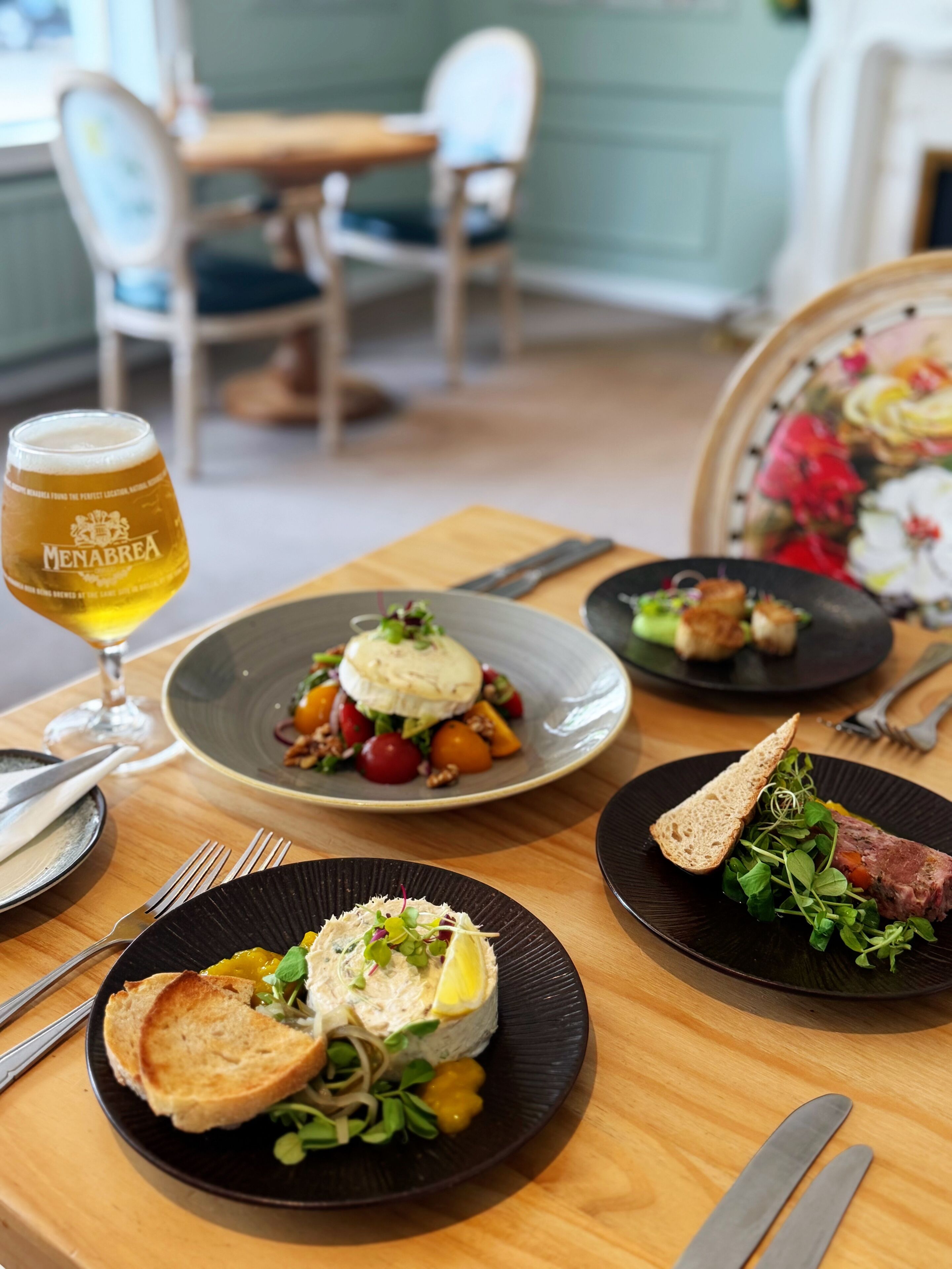 Une table à manger avec des assiettes remplies de nourriture, un verre de bière et des couverts.