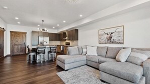 A modern living room with a gray sectional sofa, a dining area with a kitchen in the background, and a large painting of a bull on the wall.