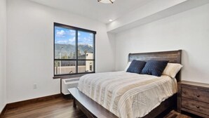 A bedroom with a large window, a bed, a bench, and a nightstand.