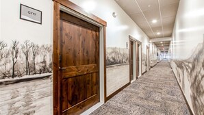 A hallway with a wooden door labeled "GYM," carpeted floors, and wall art depicting winter scenes.