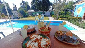 An outdoor dining table with a pool view, featuring a meal with bread, beans, and a drink. - Cabañas Elsa María (Atlautla)