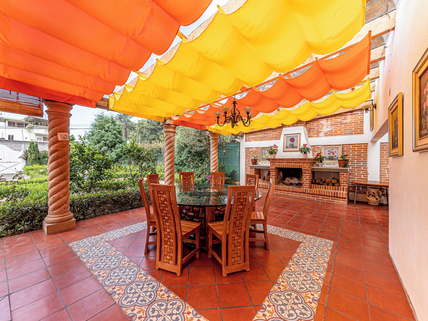Une terrasse extérieure avec une cheminée en briques, une table à manger avec des chaises et un auvent jaune.