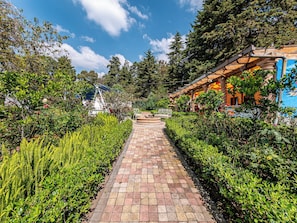 A paved pathway flanked by lush greenery and a building with a colorful facade. - Cabañas Elsa María (Atlautla)