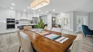 A modern kitchen with white cabinets, stainless steel appliances, and a wooden dining table with chairs. - House with Hot tub, close to Marina, in a Golf Course Community (Hertford)