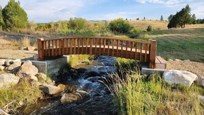 Un pont en bois enjambant un petit ruisseau, entouré de verdure et avec des collines en arrière-plan.