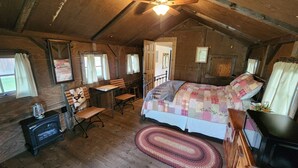 Une chambre à coucher au style rustique, avec un plafond en bois, un lit recouvert d’une courtepointe à motifs, un bureau avec une chaise et un tapis tissé.