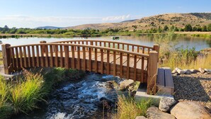 Un pont en bois enjambant une rivière, avec vue sur des collines et un bateau sur l’eau.