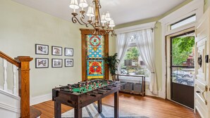 A room with a foosball table, a chandelier, a stained glass window, and framed pictures on the wall. - Amazing Location! Short North Victorian Oasis 5-bedroom w Hot Tub and Peleton (Columbus)