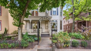 A two-story house with a front porch, steps leading to the door, and a small garden area. - Amazing Location! Short North Victorian Oasis 5-bedroom w Hot Tub and Peleton (Columbus)