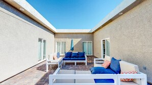 A sunlit outdoor patio with a white sofa set, a blue sofa set, and a white table.
