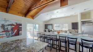 A spacious kitchen with a marble countertop, a large island with bar stools, and a high ceiling with exposed beams.