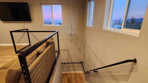A staircase with wooden steps and a metal railing, leading to a balcony with a view of the sky and landscape.