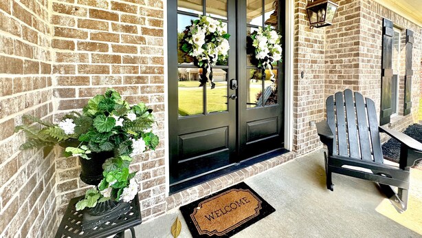 A brick exterior with a black door, a welcome mat, a potted plant, and a wooden chair outside. - The Sweet Magnolia 4BR Home by VelvetDitchVillas (Oxford)