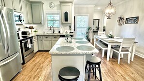A kitchen with a central island, wooden flooring, and a dining area with a chandelier. - The Sweet Magnolia 4BR Home by VelvetDitchVillas (Oxford)
