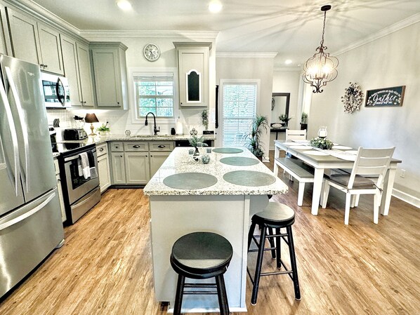 A kitchen with a central island, wooden flooring, and a dining area with a chandelier.